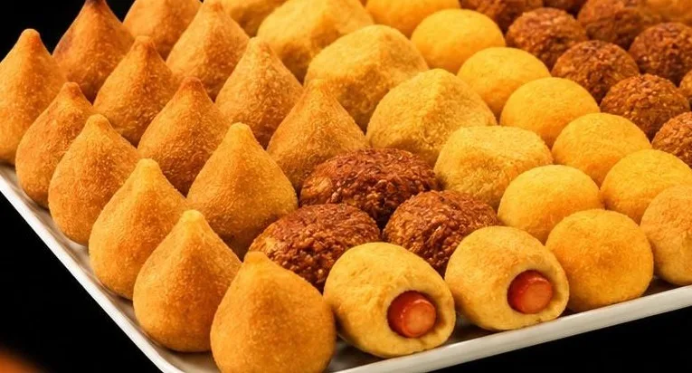 Bandeja branca com mini salgados sortidos: coxinhas, kibes, bolinhas e enroladinhos de salsicha